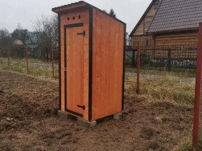 Дачный туалет из дерева возле забора, вид спереди