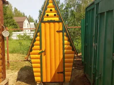 Деревянный туалет для дачи треугольной формы, установленный на бетонные блоки